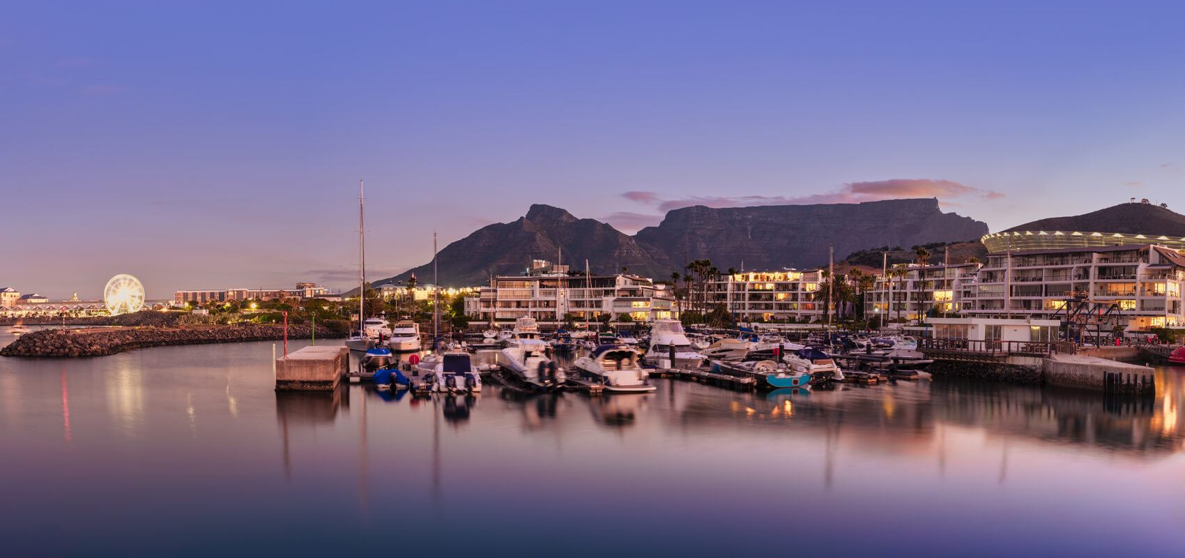 Panoramic view of the V&A Waterfront illuminated after sunset, with Table Mountain standing tall in the background.